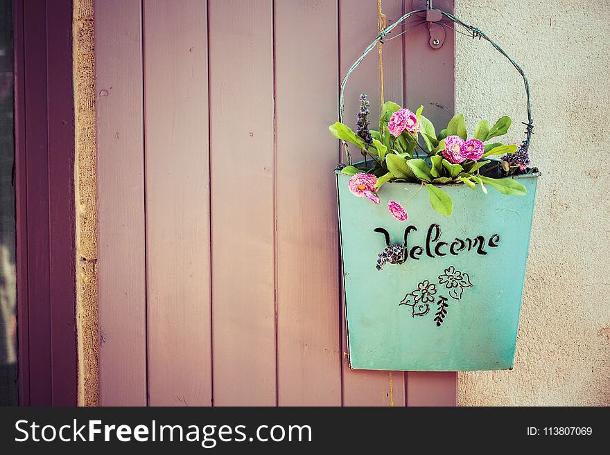 loseup of green basket with fresh flowers and welcome sign text written in black on wall near door. loseup of green basket with fresh flowers and welcome sign text written in black on wall near door