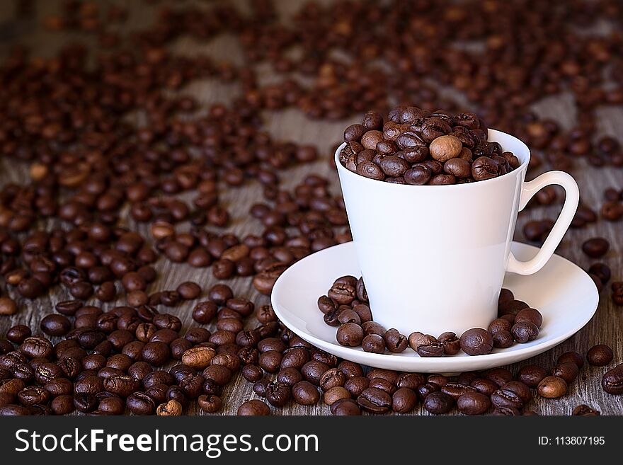 Coffee concept: fried coffee beans in porcelain white coffee cup. Dark background