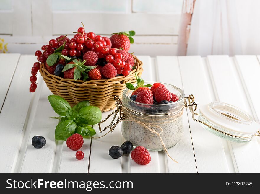 Healthy blended smoothie made from almond milk. Glass jar with chia pudding with fresh strawberries, raspberries and blueberries. Basket with berries. On a wooden light background.