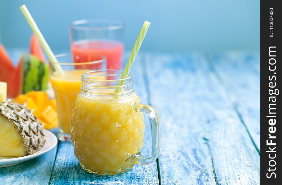 Fresh pineapple and watermelon smoothie in three glasses on a blue wooden rustic background. Freshly blended summer smoothie nice to drink during a hot day.