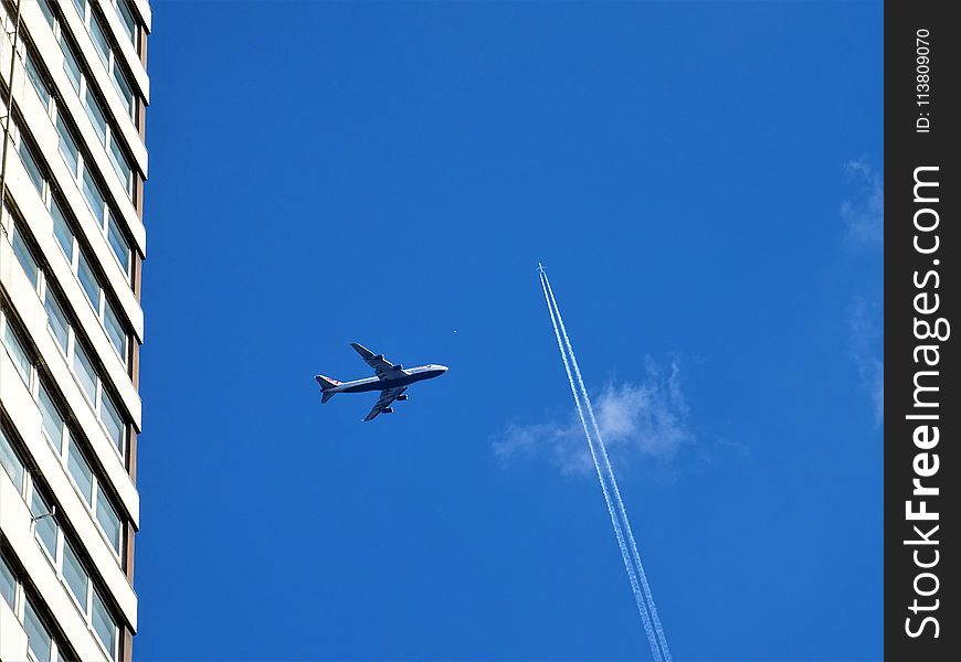 Low-angle Photography of White Plane on Mid-air Near White Concrete Building and White Contrail
