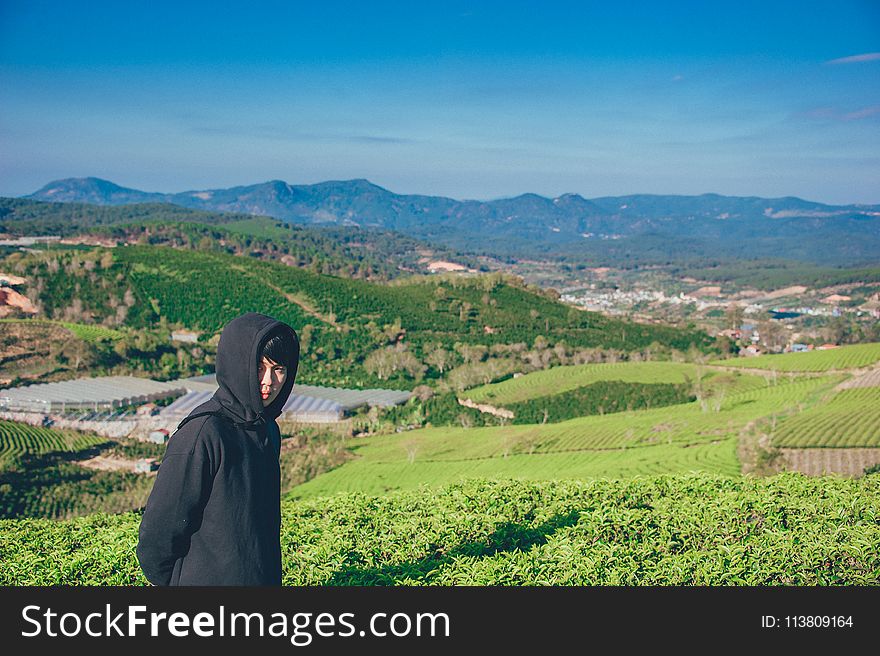 Man Wearing Hoodie Taking Picture With Mountain and Field Photography