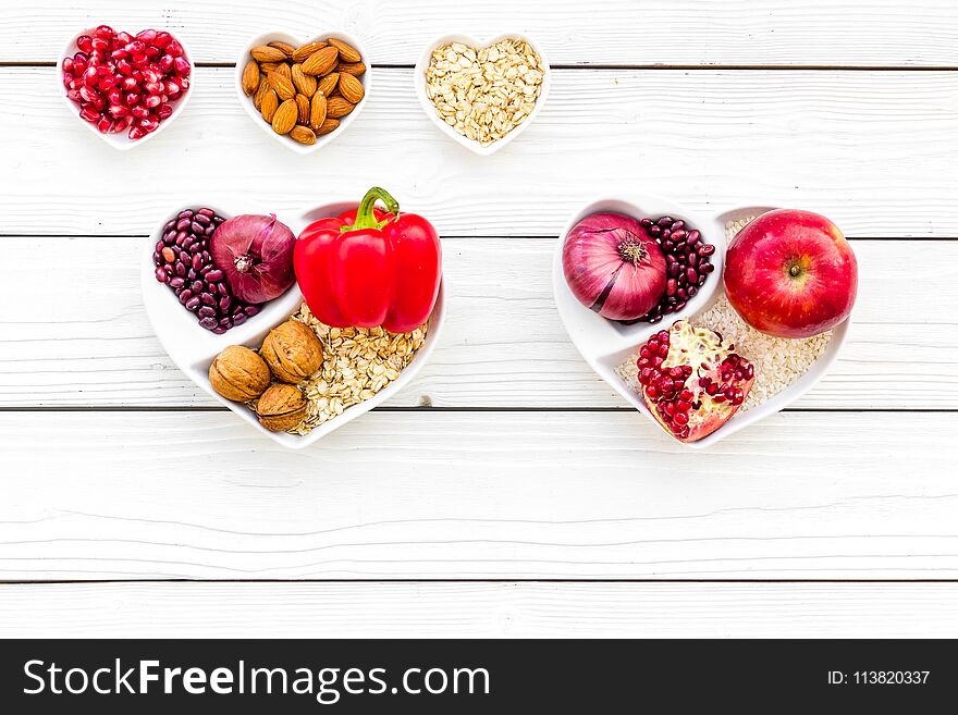 Diet for healthy heart. Food with antioxidants. Vegetables, fruits, nuts in heart shaped bowl on white background top view.