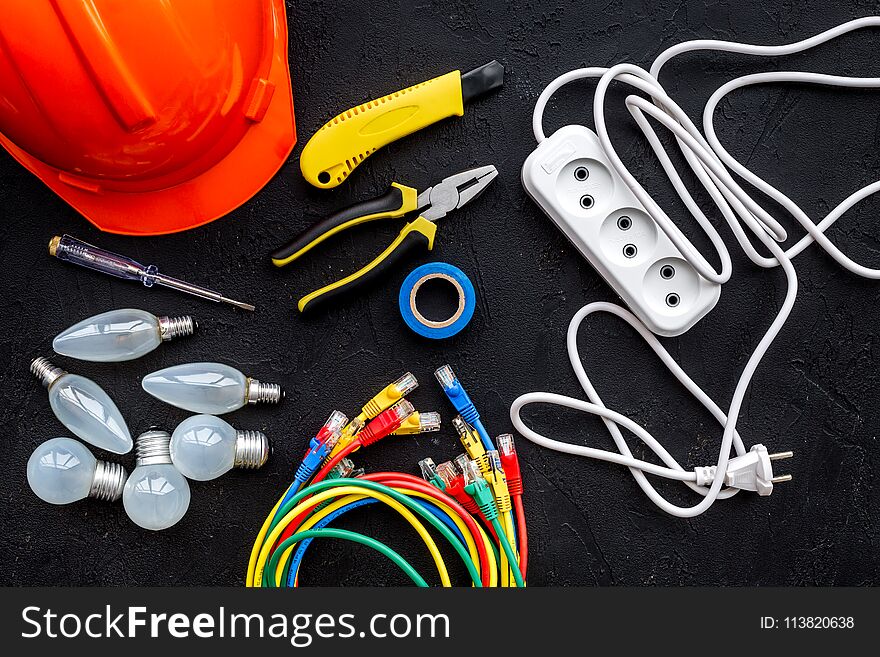 Electrician work concept. Hard hat, tools, cabel, bulb, socket outlet on black background top view.