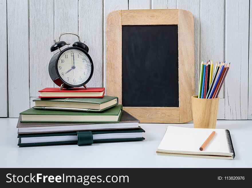 Education workspace background concepts alarm clock, Color Pencil, crayons in wooden cup and exercise books and Chalkboard with White wooden vintage wall. back to school concepts. Education workspace background concepts alarm clock, Color Pencil, crayons in wooden cup and exercise books and Chalkboard with White wooden vintage wall. back to school concepts