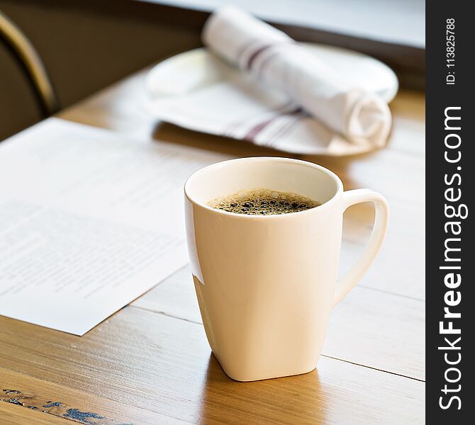 Cup of freshly brewed coffee on a restaurant table with a menu in the background