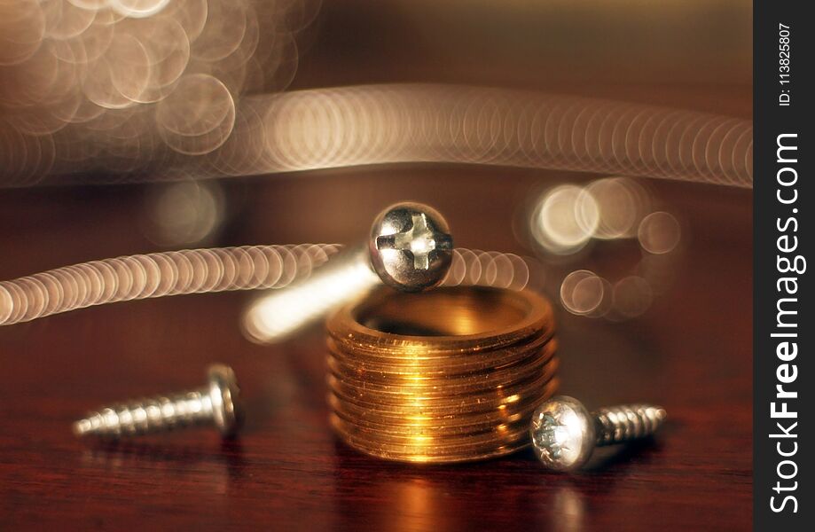 Metal bolts, screws, lying on table and a bronze part with thread and bokeh