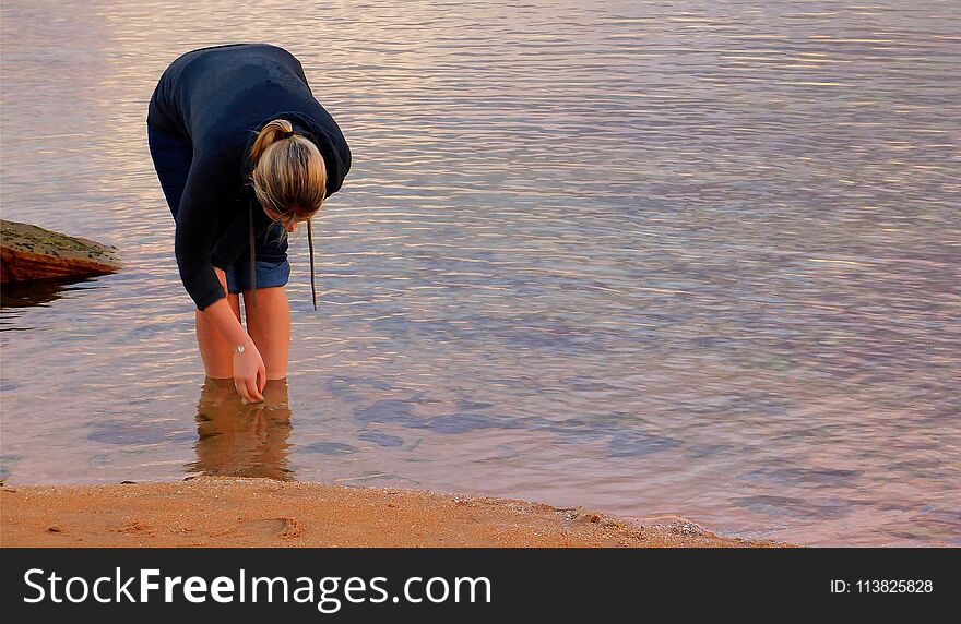 Blonde Girl Picking Up Shells From A Pond