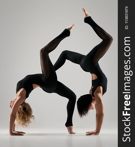 Beautiful flexible women doing partner yoga on grey background. Beautiful flexible women doing partner yoga on grey background