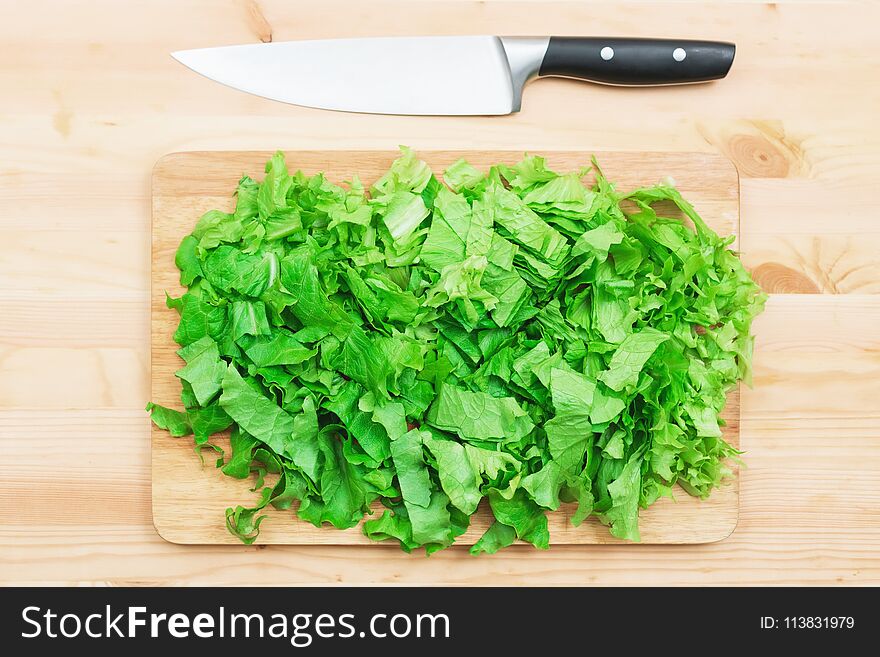 Close-up on a wooden table is a wooden cutting board on which lies chopped lettuce leaves and next to a large cutting knife. The concept of self-cooking vegetarian food at home. Healthy lifestyle.