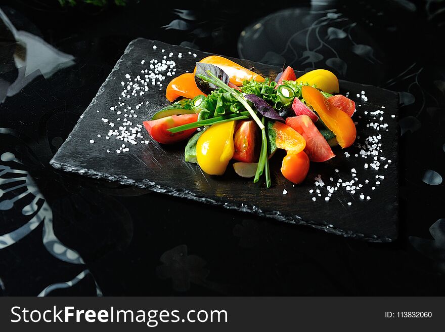 Sliced vegetables on a wooden board in a restaurant, cucumbers, tomatoes, peppers, lettuce leaves.