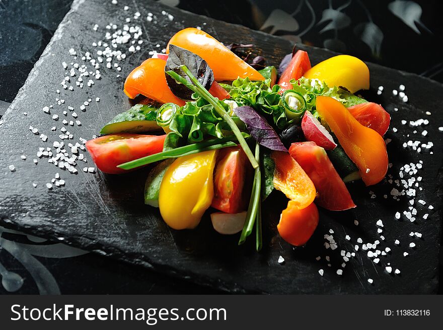 Sliced vegetables on a wooden board in a restaurant, cucumbers, tomatoes, peppers, lettuce leaves.