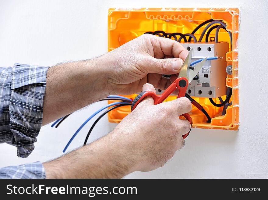 Electrician technician at work on a residential electrical panel, prepares the cable with professional scissors. Electrician technician at work on a residential electrical panel, prepares the cable with professional scissors