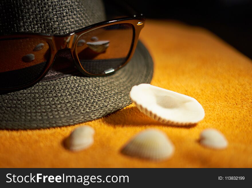 Sun glasses, striped hat and sea shells on an orange towel.