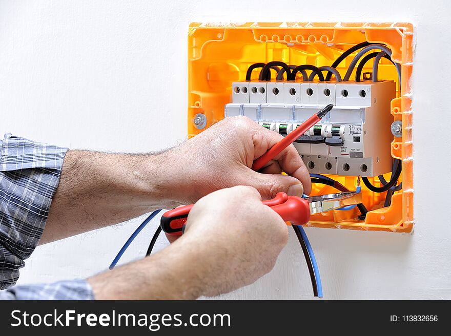 Electrician technician working on a residential electric panel, he inserts the cable in the magnetothermic switch terminals. Electrician technician working on a residential electric panel, he inserts the cable in the magnetothermic switch terminals