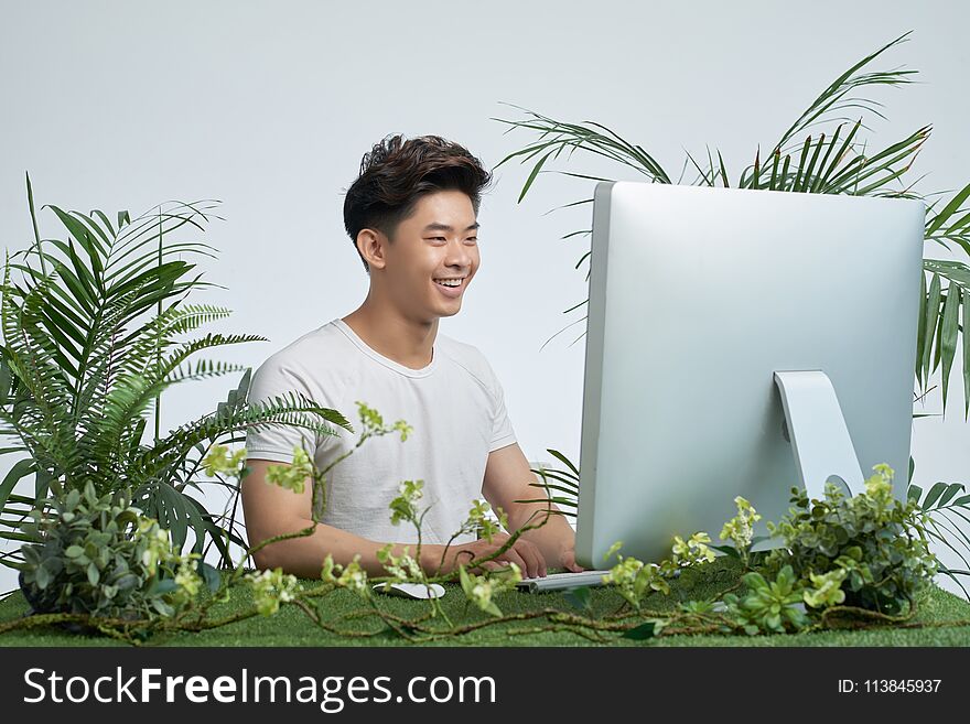 Happy excited Vietnamese young man working on computer with various plants around his workplace. Happy excited Vietnamese young man working on computer with various plants around his workplace