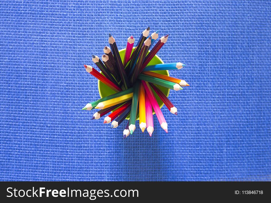 Set of colored pencils in a glass on a blue background, top view