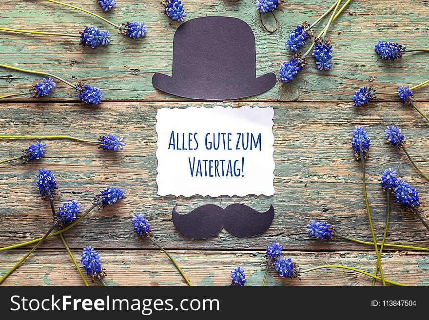 Father`s Day card with cardboard hat and mustache and blue flowers. German greeting `Alles gute zum Vatertag!`, which means `Happy Father`s Day`.