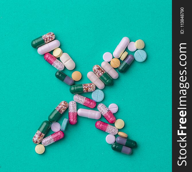 Pills laid out in the shape of a cross or X on a green background. Conceptual for pharmaceutical production.