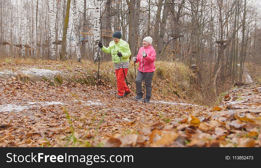 Fitness for elderly women in autumn park - nordic walking among autumn park, telephoto shot