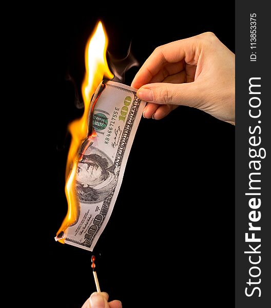 One hundred dollars burn in the hand on a black background .
