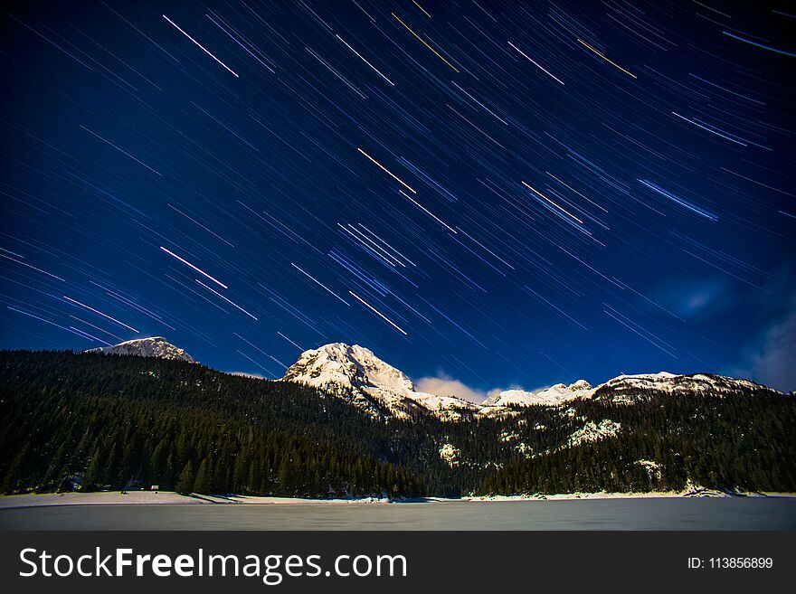 Long exposure night sky with beautiful star trails above mountain with snow and forest. Long exposure night sky with beautiful star trails above mountain with snow and forest