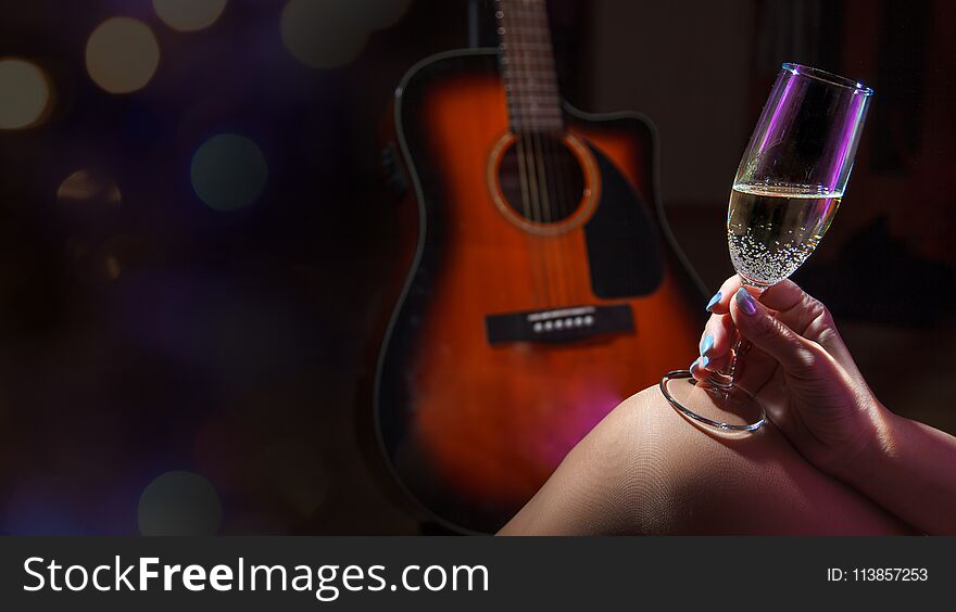 Female hand holding a glass of champagne on dark background with acoustic guitar