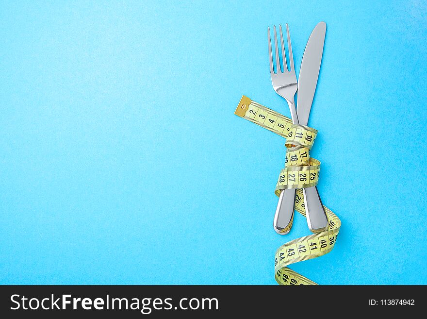 Diet menu in the restaurant or cafe. The fork and knife are wrapped in yellow measuring tape on blue background. Copy space for text