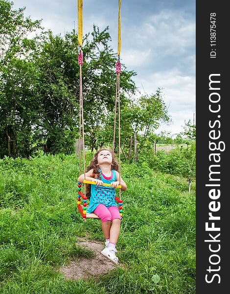 Happy baby girl having fun on swing on summer day, sitting on swing looking up at the sky. Happy baby girl having fun on swing on summer day, sitting on swing looking up at the sky