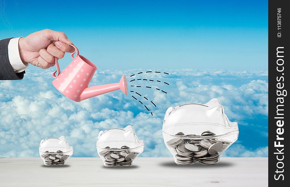 Transparent piggy bank filled with coins on wood background.Saving investment concept.Watering can and money growth drawn concept