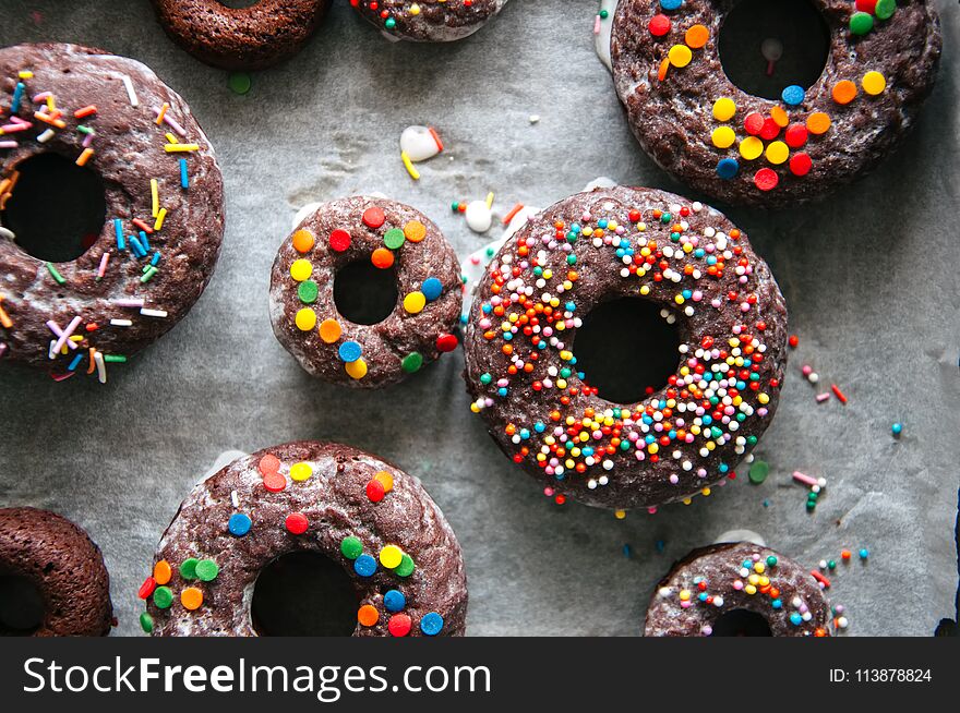 Baked chocolate doughnuts with glaze and confectionary topping on a baking paper Top view.