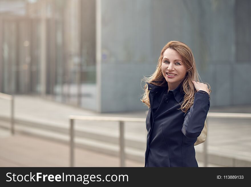 Happy smiling woman standing in the wind on an urban street with her long blond hair blowing around her face with lateral copy space