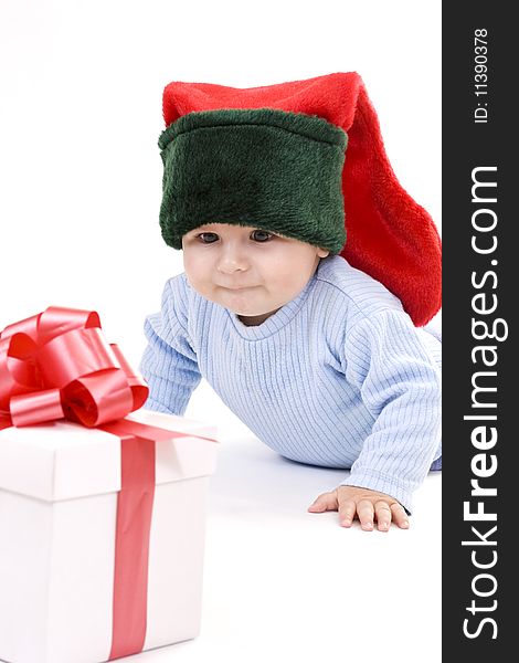 A baby wearing at elves hat looking at a gift. A baby wearing at elves hat looking at a gift