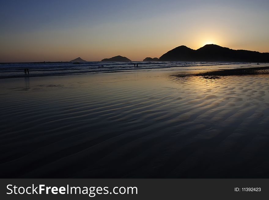 Sunset at the Baleia Beach in Brazil, with golden reflexion from the sun in the ocean and people enjoying the end of the afternoon. Sunset at the Baleia Beach in Brazil, with golden reflexion from the sun in the ocean and people enjoying the end of the afternoon