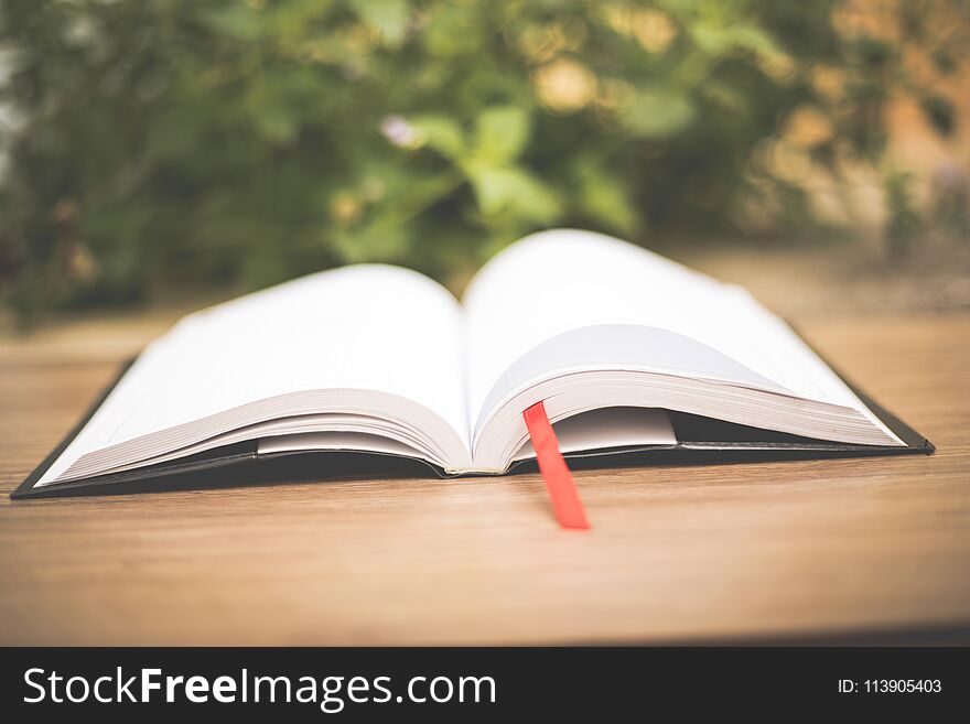 An open book on wooden table at home garden with nature bokeh background