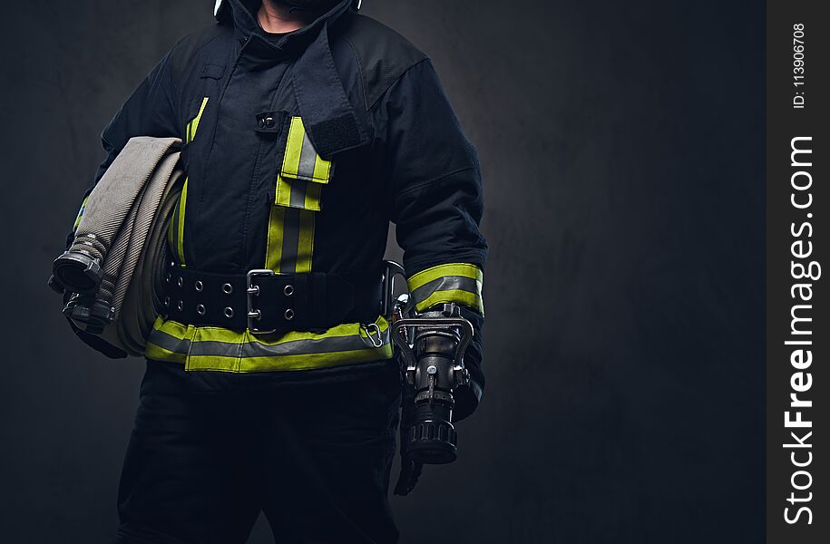 Studio portrait of a firefighter in uniform holds fire hose.