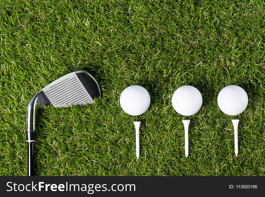 Golf club and three balls lie beautifully on the green grass