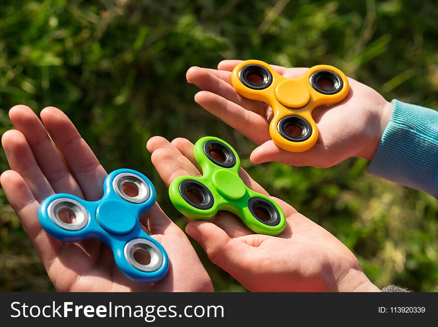 Spinner of different colors lie in the hands of children against the background of grass