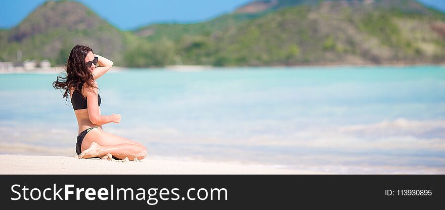 Woman sitting on beach laughing and enjoying summer holidays looking at the camera. Beautiful model in bikini sitting