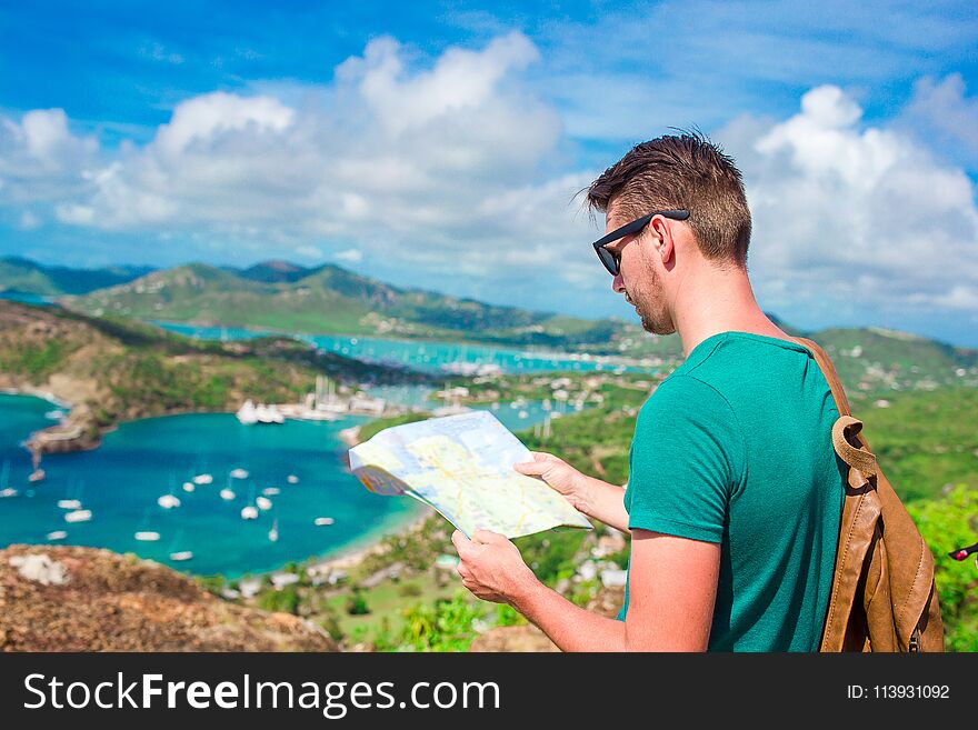 Young Tourist Man With Map Background Of English Harbor From Shirley Heights, Antigua, Paradise Bay At Tropical Island