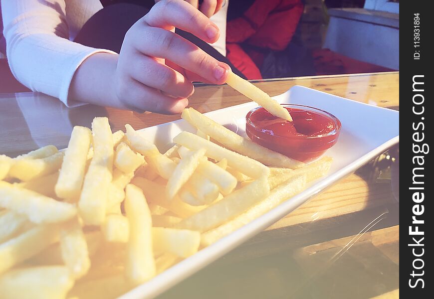 French Fries in the white plate with red cachup, girl hold one piece of french fries in her fingers.