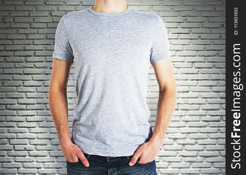 Man wearing blank grey shirt on brick wall background. Advertisement and design concept. Mock up. Man wearing blank grey shirt on brick wall background. Advertisement and design concept. Mock up