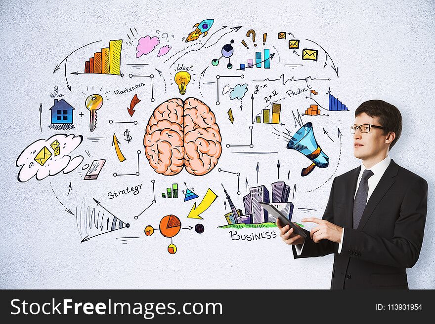 Handsome european businessman using tablet on concrete wall background with business brain sketch. Brainstorming, success and plan concept