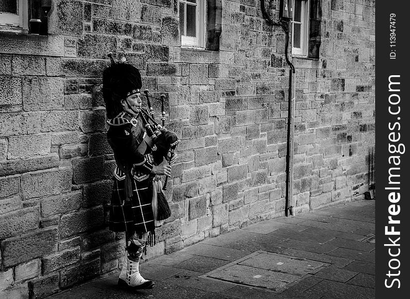 Person Using Bagpipes Near Wall in Grayscale Photography