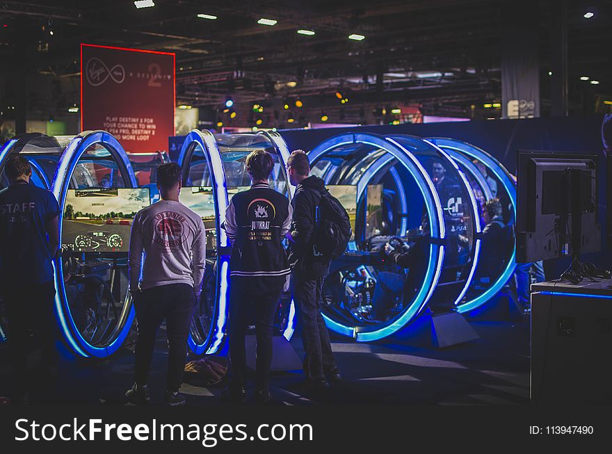 Three Men Standing in Front of Racing Arcade Machines