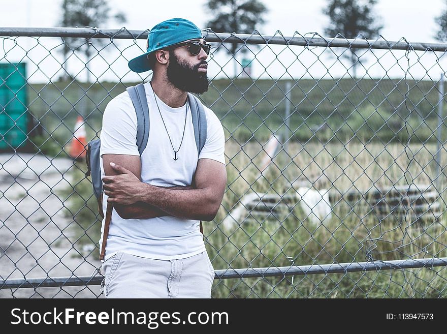 Selective Focus Photography of Man in White Crew-neck T-shirt Leaning on Gray Metal Chain Fence