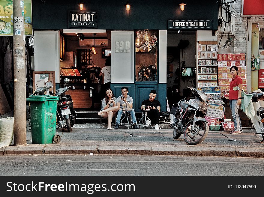 Three People Sitting on Chairs Outside Coffee & Tea House Near Motorcycles