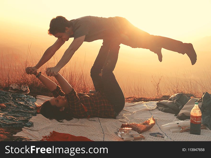 Woman Lying on Blanket Under Man on Her Legs Holding Hands during Golden Hour