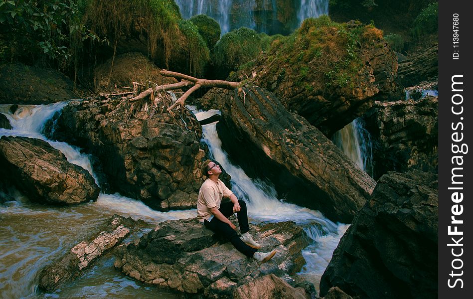 Photo Of Man Sitting On Gray Rock Surrounded By Water Falls