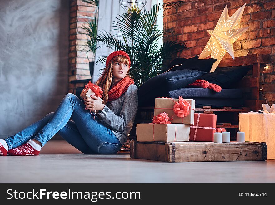 Redhead female holds a Christmas gift in a living room with loft interior. Redhead female holds a Christmas gift in a living room with loft interior.